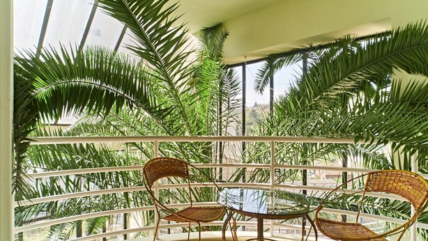 A balcony with a glass table and wicker chairs, surrounded by lush green foliage. - S&L Boutique Hotel  (Tbilisi)