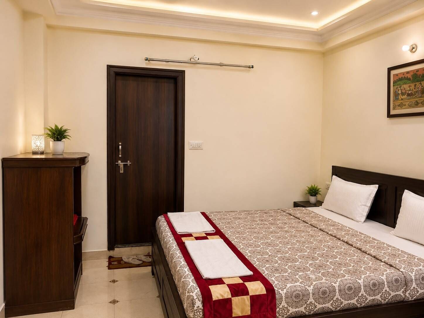 A bedroom with a bed, a wardrobe, a door, a nightstand, and a wall-mounted light fixture.
