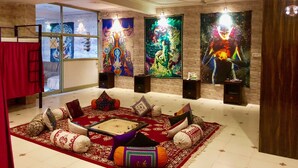Quarto com tapete vermelho, uma pequena mesa e obras de arte coloridas nas paredes.