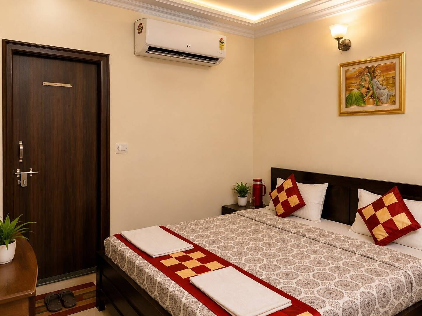 A hotel room with a bed, a nightstand, a potted plant, an air conditioner, and a door.