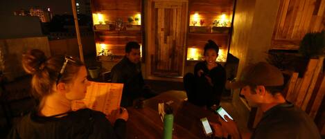 A group of people seated around a wooden table in a dimly lit room with wooden shelves and plants.
