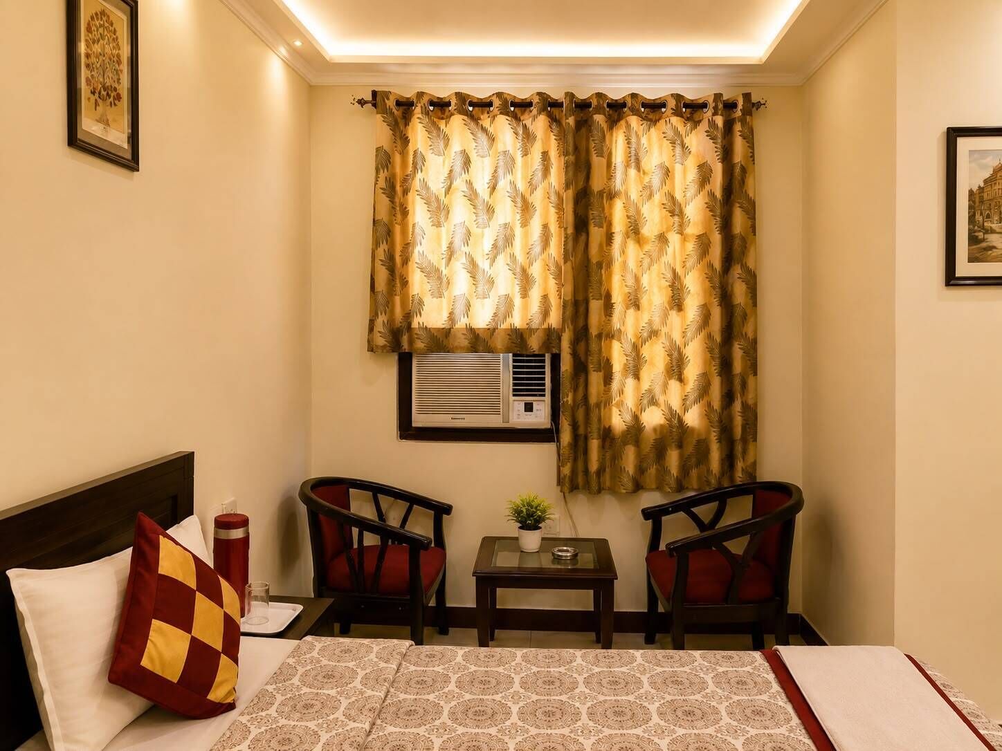 A hotel room with a bed, two chairs, a small table, and a window with curtains.