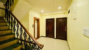 Uma escadaria com grades de metal decorativas leva a um patamar com duas portas de madeira e um interruptor na parede.