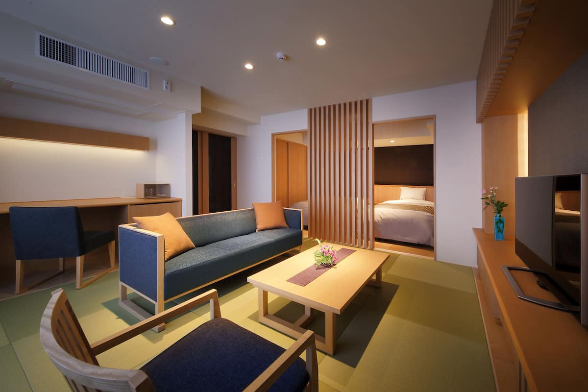 Ein modernes Hotelzimmer mit einer Couch, einem Esstisch, einem Fernseher und einem separaten Schlafbereich.