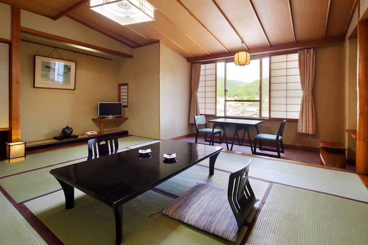 Ein traditioneller japanischer Raum mit Tatami-Bodenbelag, einem niedrigen Tisch und einem Fernseher auf einem Standfuß.