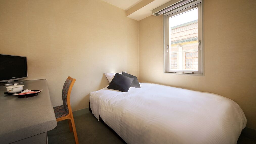 Une chambre d’hôtel avec un lit, un bureau avec une télévision, une chaise et une fenêtre.