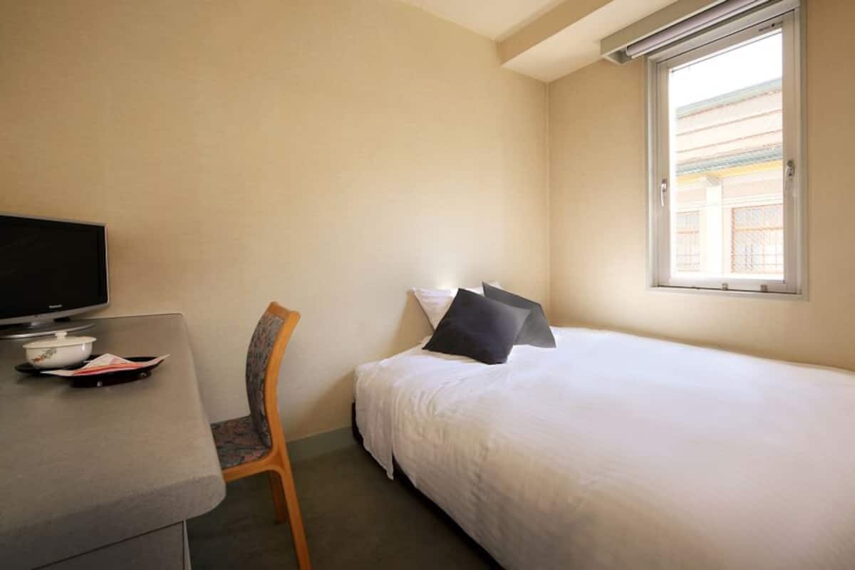 Ein Hotelzimmer mit einem Bett, einem Schreibtisch mit Fernseher, einem Sessel und einem Fenster.
