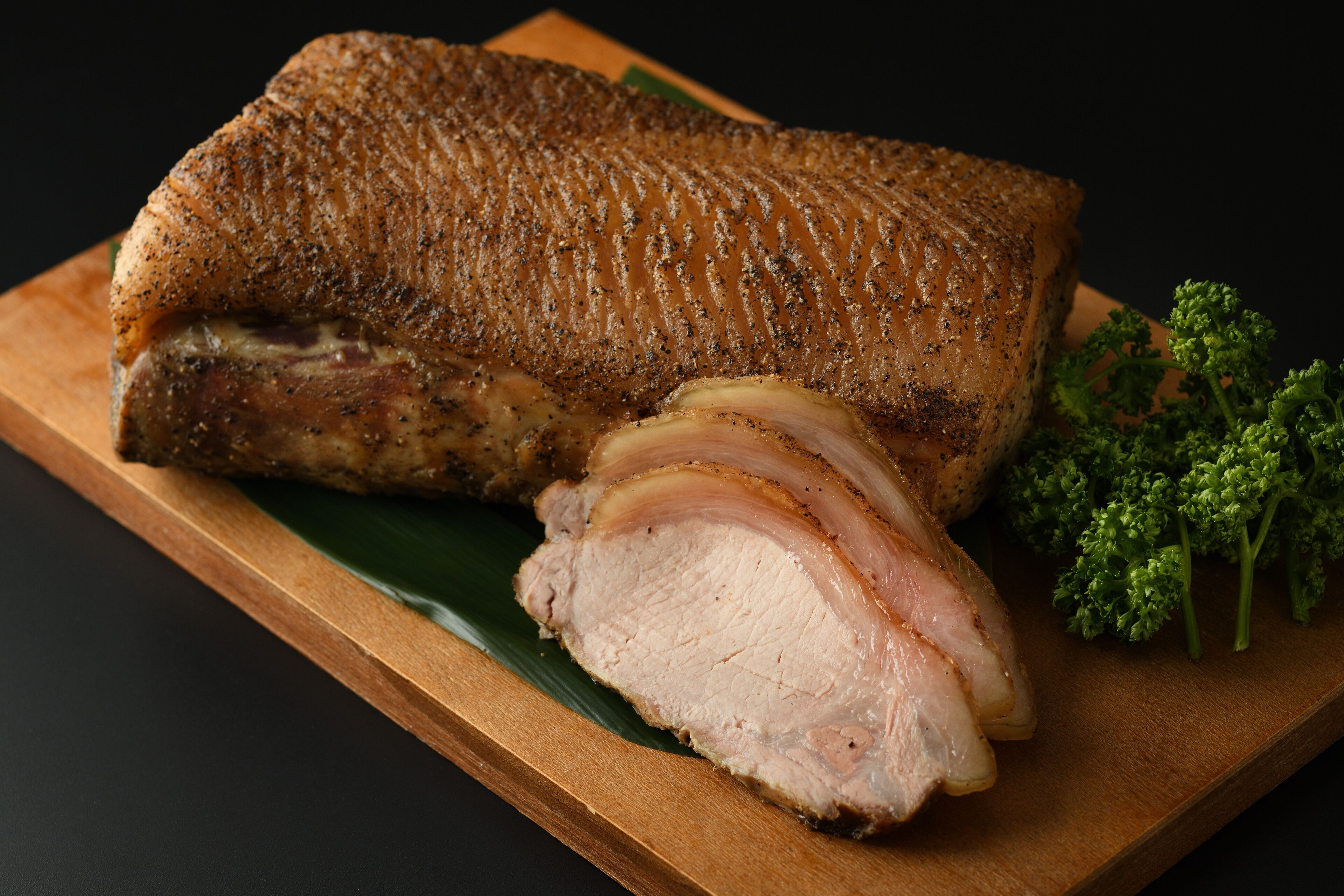 A roasted pork loin on a wooden board with a green leaf underneath.