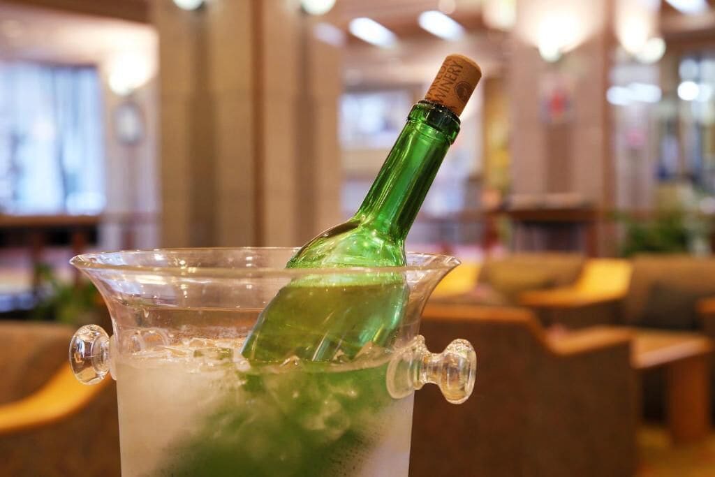 Een groene fles in een glazen karaf met kurk, geplaatst in een bar met houten meubels.