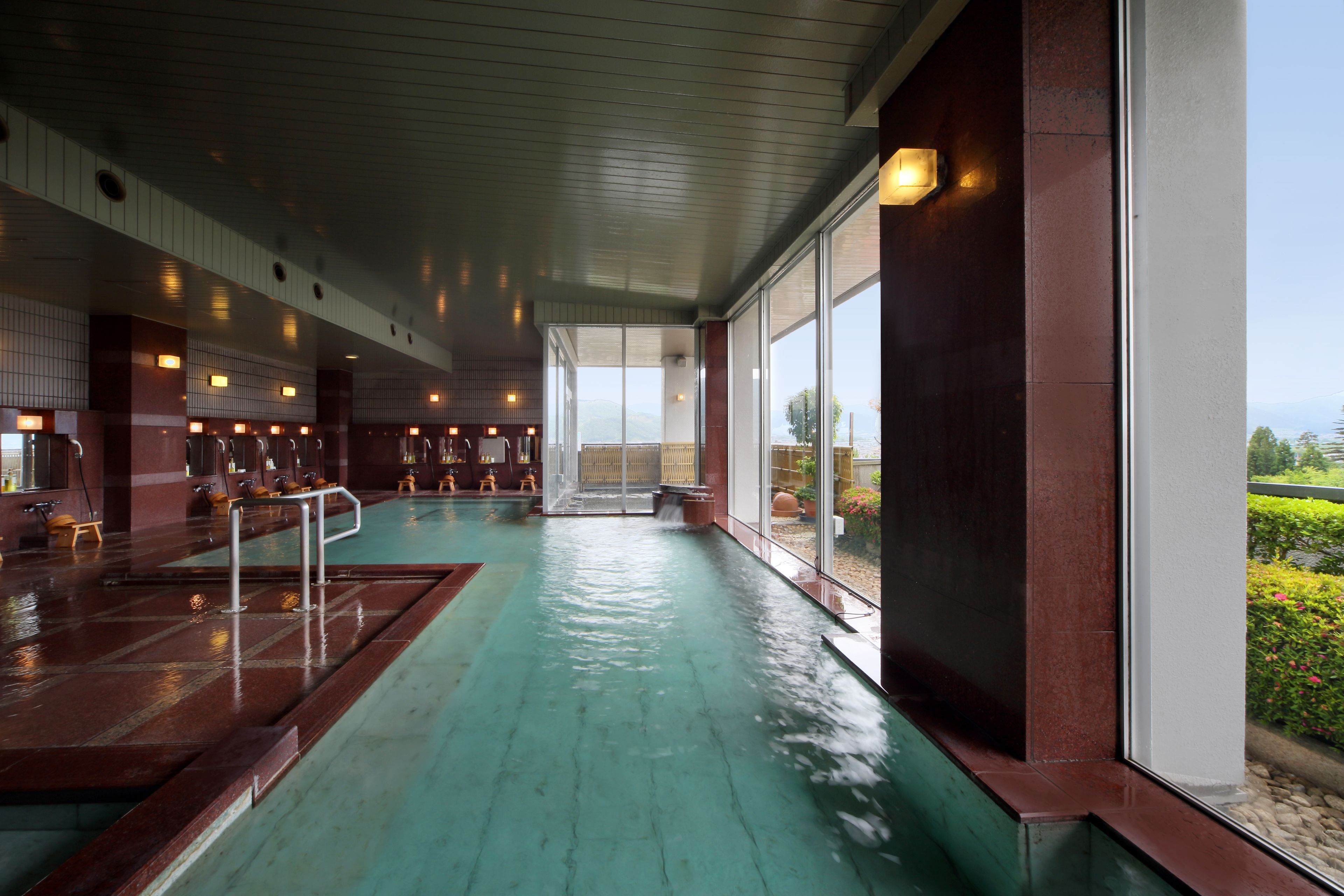 A spacious indoor swimming pool with a view of the outdoors, surrounded by wooden walls and benches.