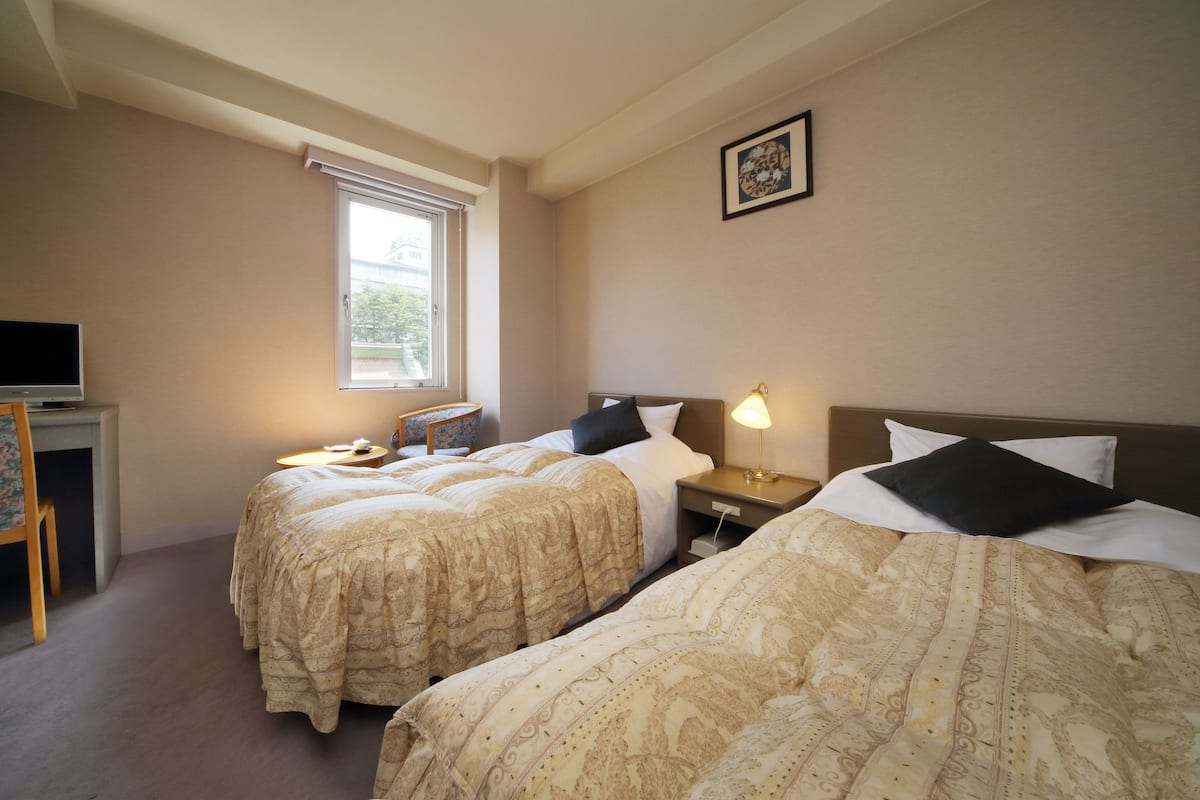 Ein Hotelzimmer mit zwei Betten, einem Schreibtisch, einem Sessel, einem Fernseher und einem Fenster.