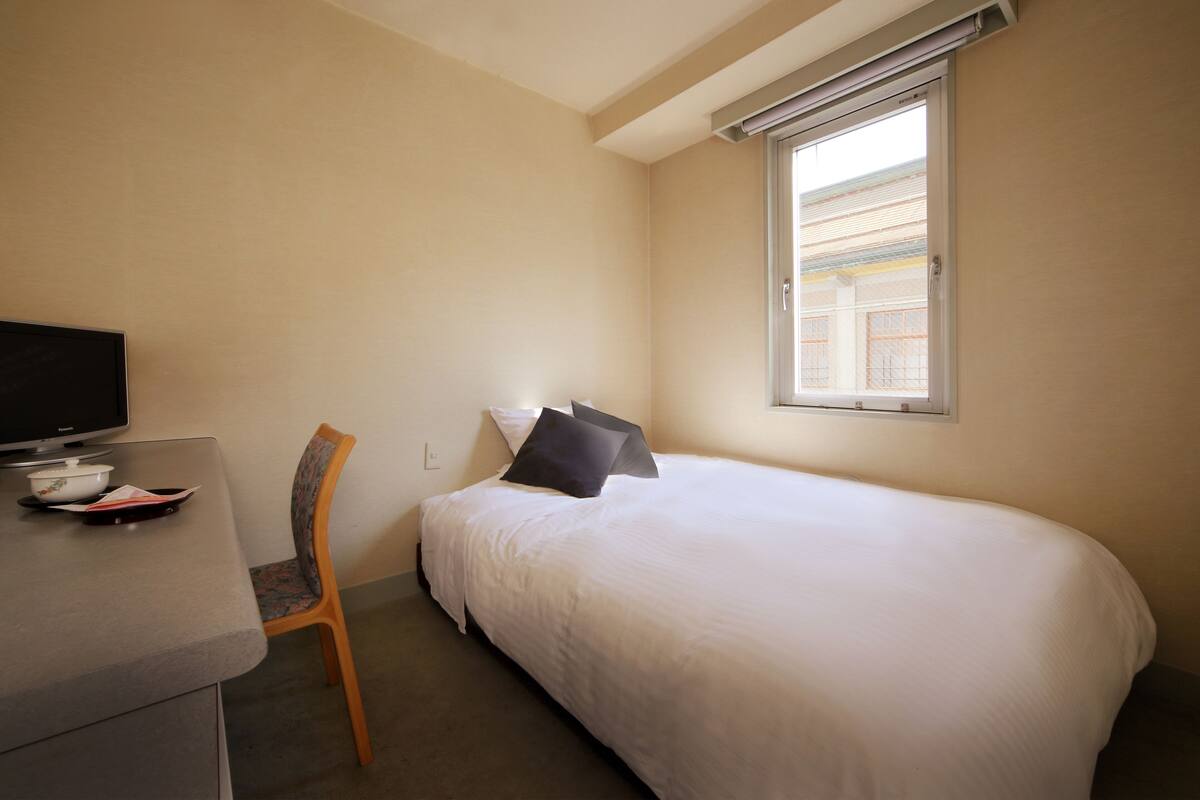 Ein Hotelzimmer mit Bett, Schreibtisch mit Fernseher und Fenster mit Jalousien.