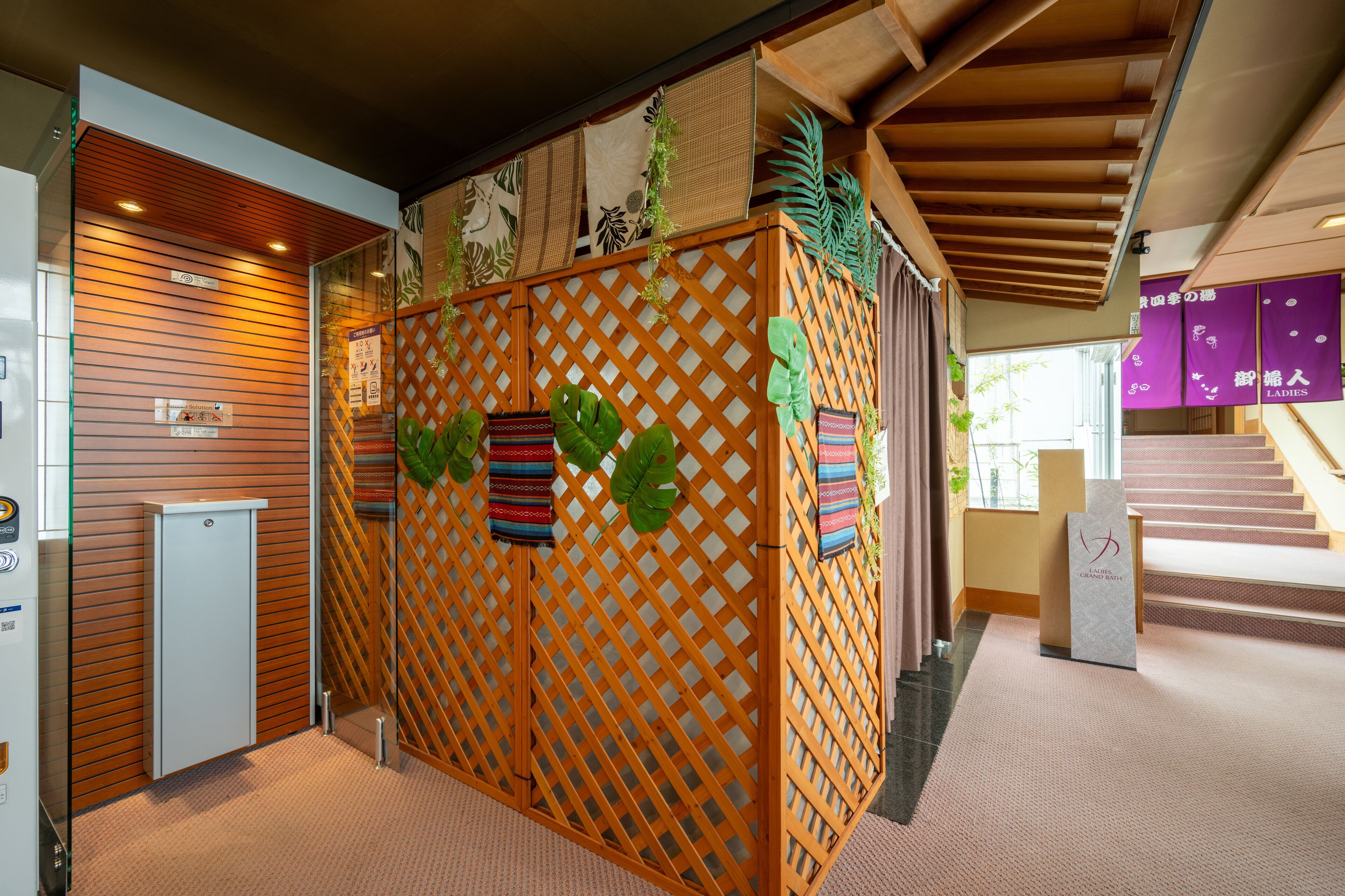 A reception area with a wooden partition, a small refrigerator, and a staircase leading to a landing with purple banners.