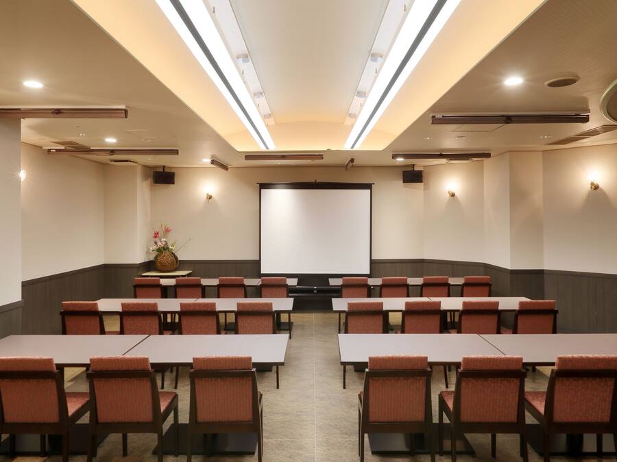 Una sala de conferencias con una pantalla grande, varias mesas y sillas dispuestas para reuniones.