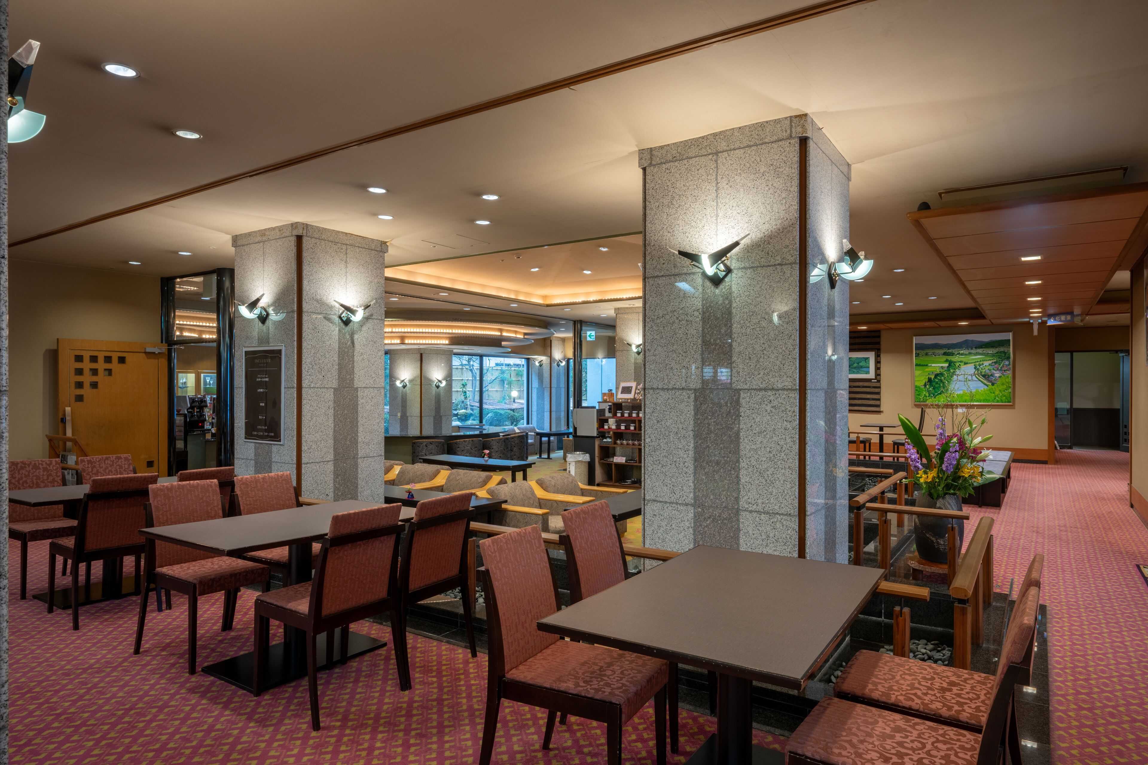 A hotel lobby with seating areas, a reception desk, and a large window offering a view.