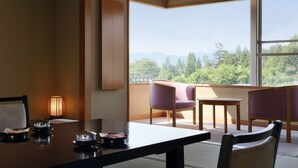 A room with a dining table, chairs, a lamp, and a view of trees and mountains through large windows. - Kaminoyama Azumaya (Kaminoyama)