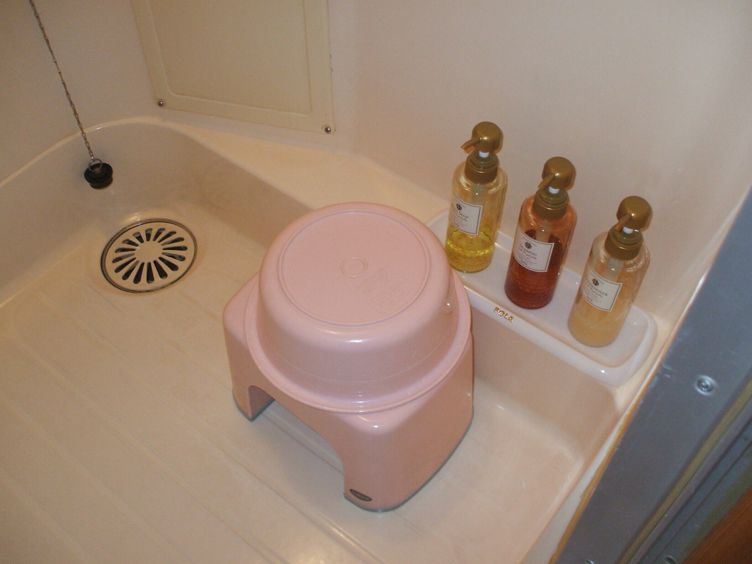 Une salle de bain avec un tabouret rose, un lavabo et trois bouteilles de savon liquide sur une étagère.