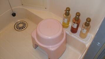 Une salle de bain avec un tabouret rose, un lavabo et trois bouteilles de savon liquide sur une étagère.
