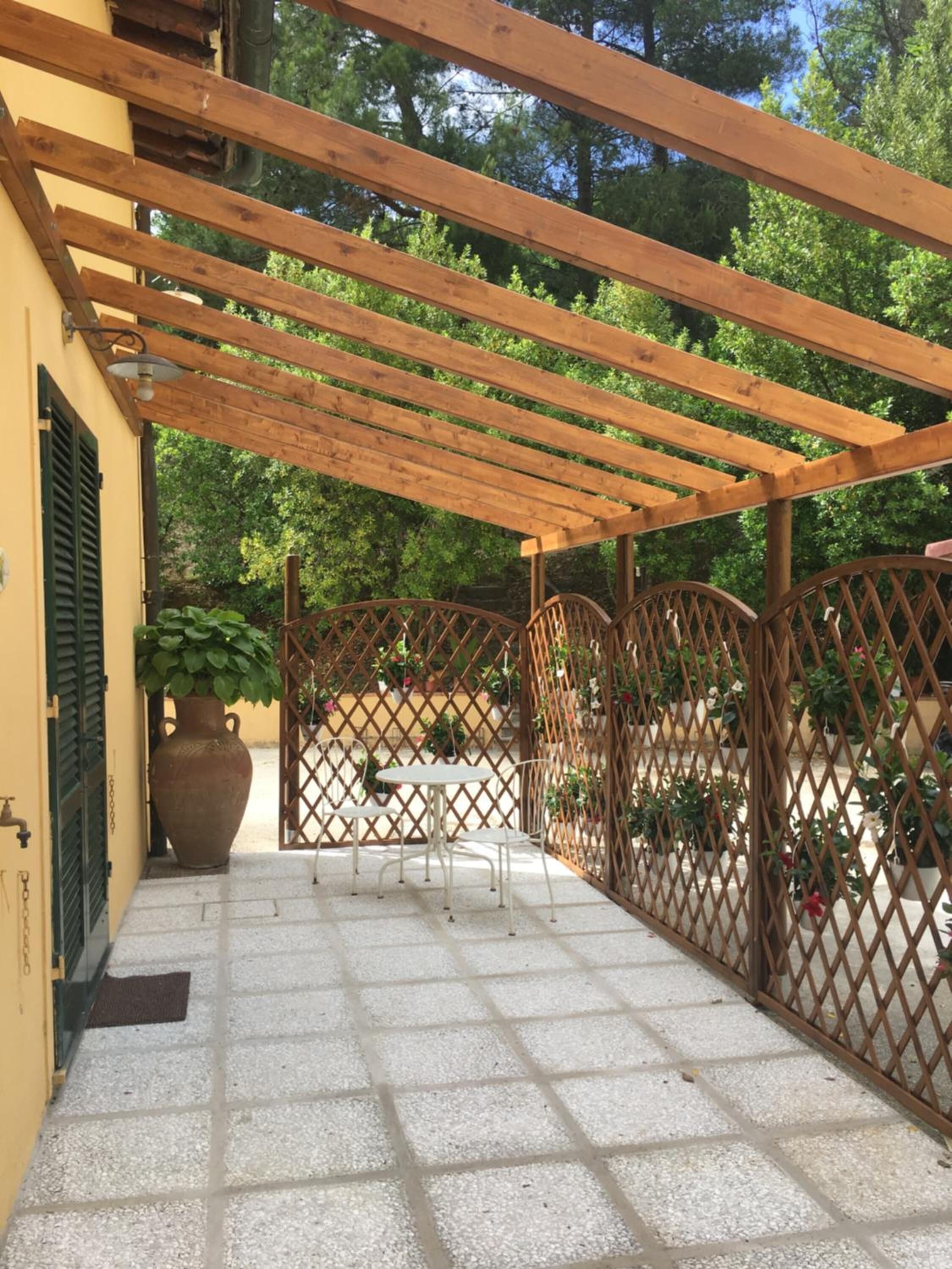 Eine überdachte Terrasse mit einer Pergola, einem Tisch, Stühlen und einem Zierzaun.