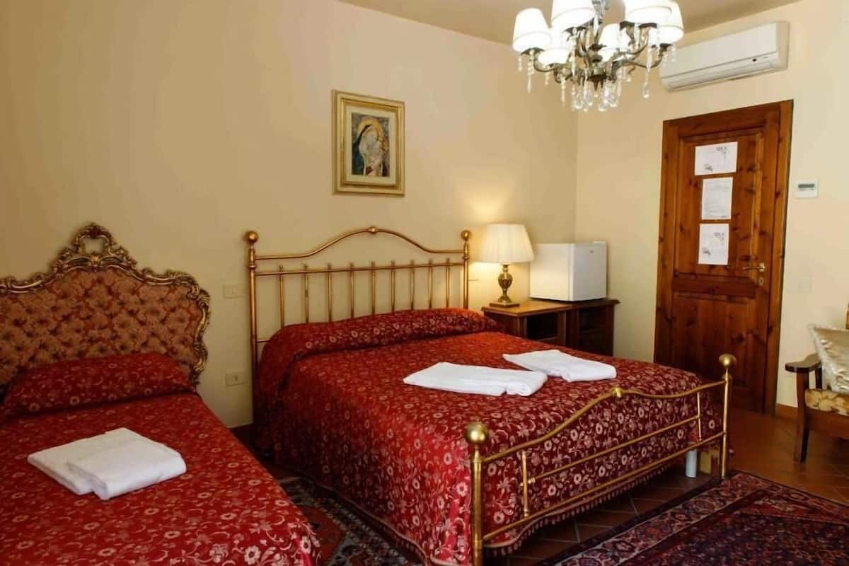 A hotel room with two beds, a chandelier, a wooden door, and a small table with a lamp.