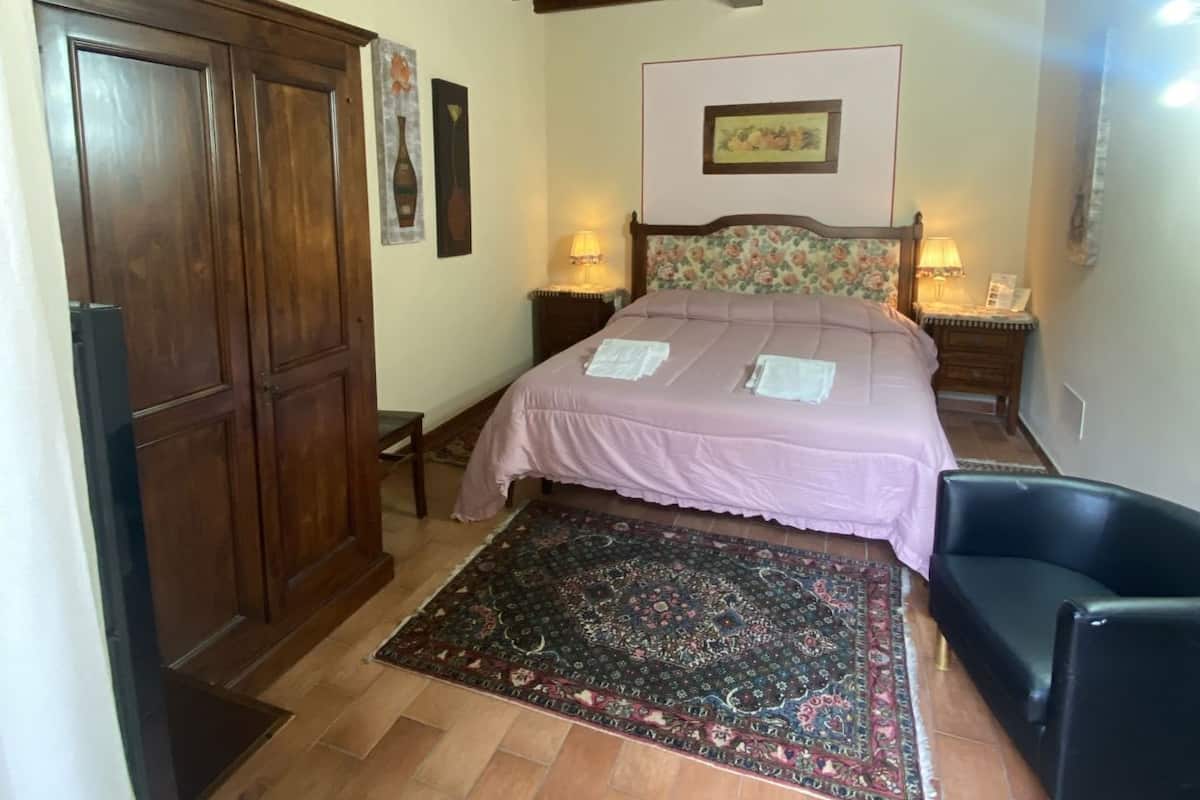 A bedroom with a wooden ceiling, a bed with a floral headboard, a nightstand, a chair, and a wardrobe.