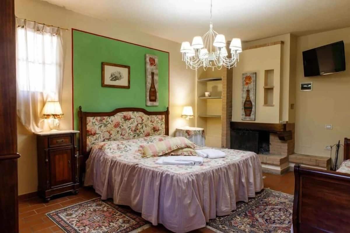 A bedroom with a round bed, a chandelier, a fireplace, and a television on the wall.