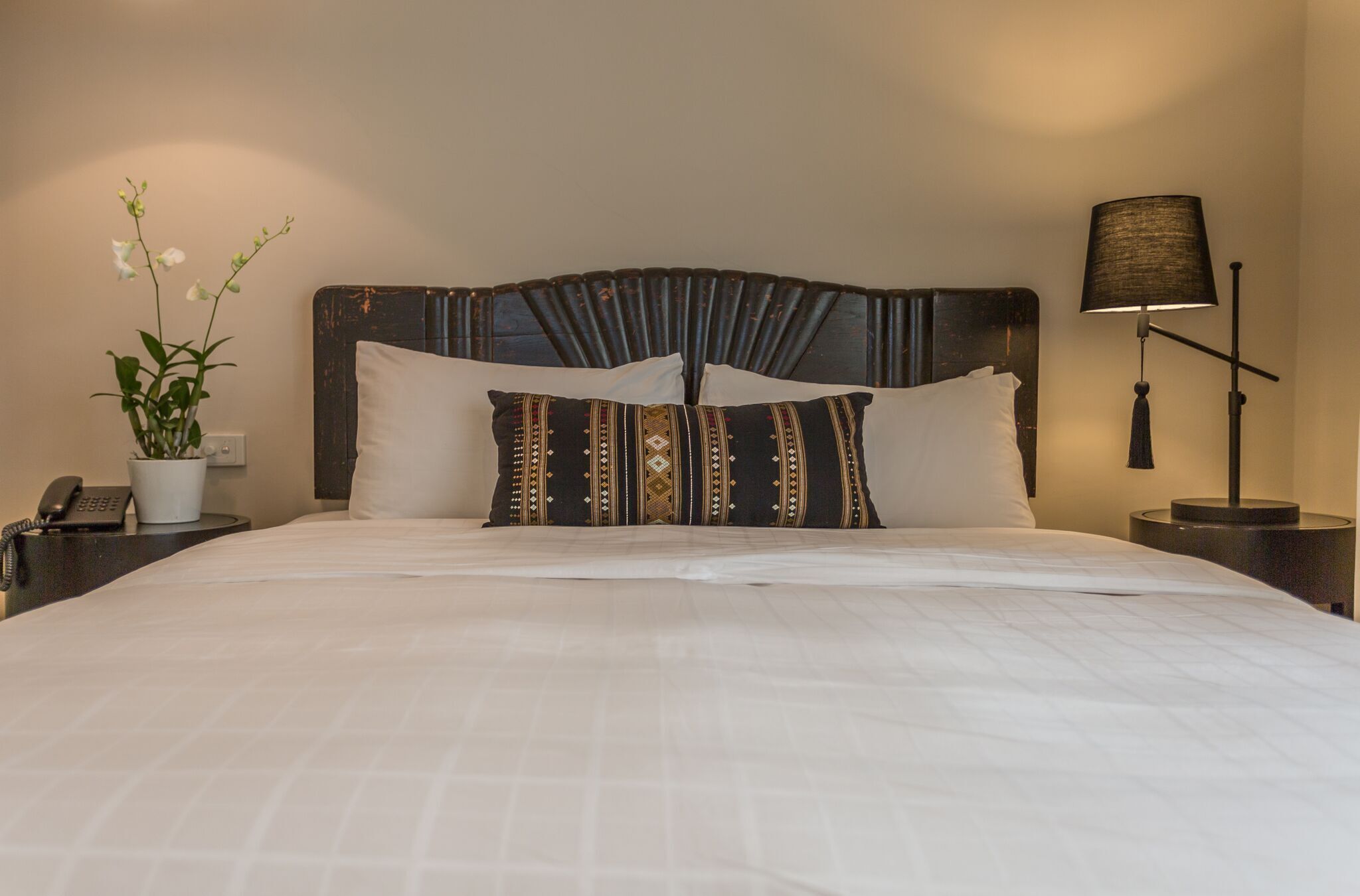 Una cama bien hecha con sábanas blancas, un cabecero decorativo y una lámpara de noche.