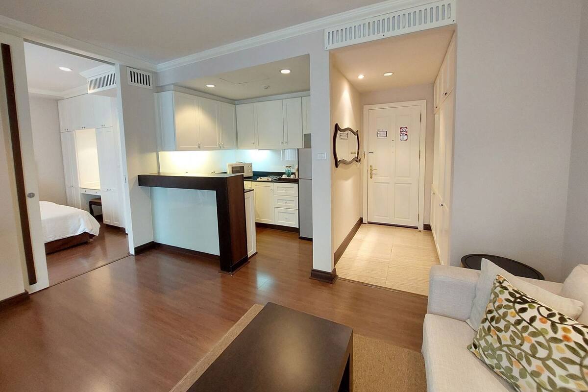 A hotel room with a bed, a sofa, a small table, a kitchenette, and a bathroom.