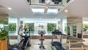 Une salle de sport moderne équipée d’appareils de cardio, de poids et offrant une vue sur l’extérieur grâce à de grandes fenêtres.