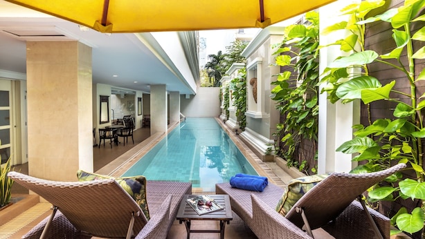 Un espace aménagé au bord de la piscine, avec des meubles en osier et un parasol jaune, entouré d’une végétation luxuriante et d’une piscine à l’eau claire.