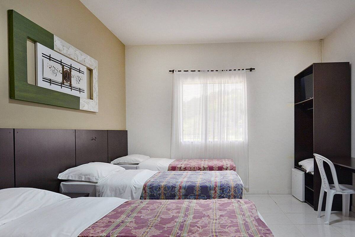 Habitación de hotel con dos camas, un escritorio, una silla, un armario y una ventana con cortinas.