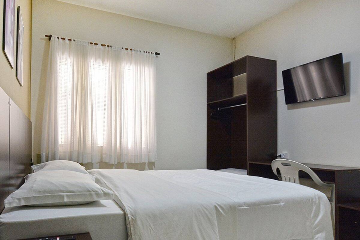 Habitación de hotel con cama, escritorio, silla, televisor y armario.