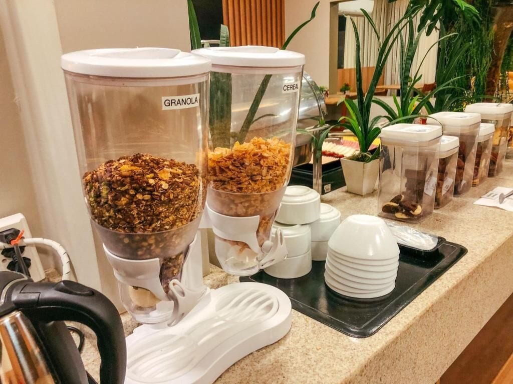 A breakfast bar with granola and cereal dispensers, white cups, and a black tray.