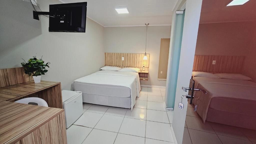 Una camera d'albergo con un letto, una scrivania, una sedia, un tavolino, una pianta in vaso e una TV a parete.