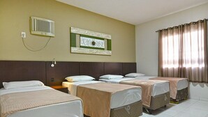A hotel room with four beds arranged in a row, a wall-mounted air conditioner, a framed artwork, and a window with curtains. - Presto Hotel (Blumenau)