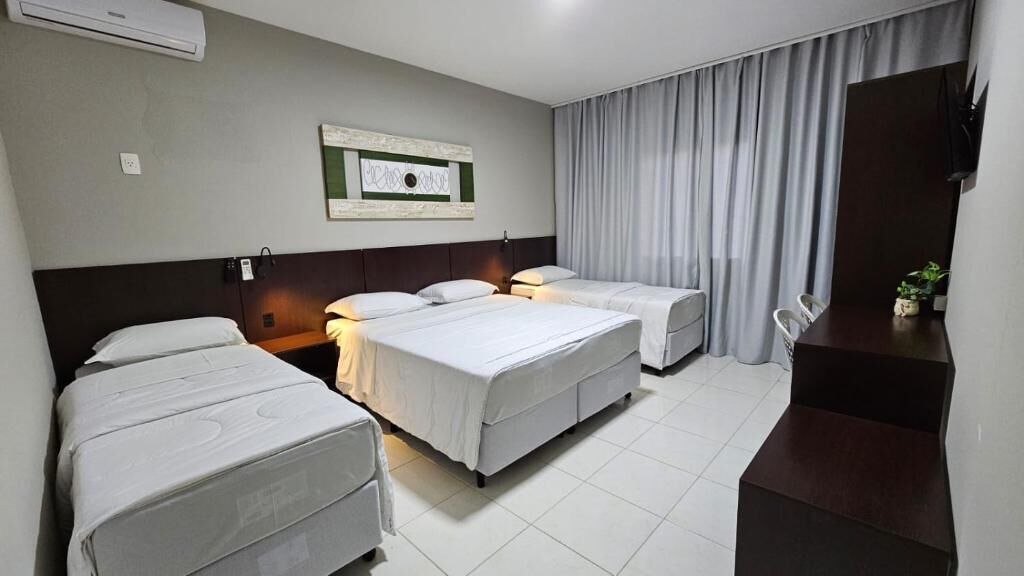 A hotel room with two beds, a desk, a chair, and a large window with curtains.