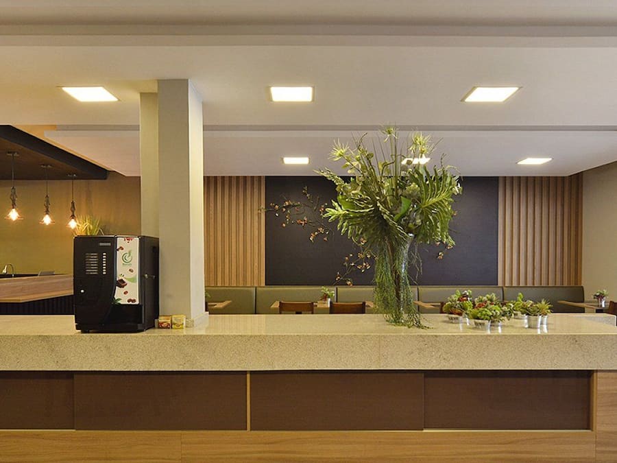 A modern hotel lobby with a reception desk, seating area, and a large plant centerpiece.