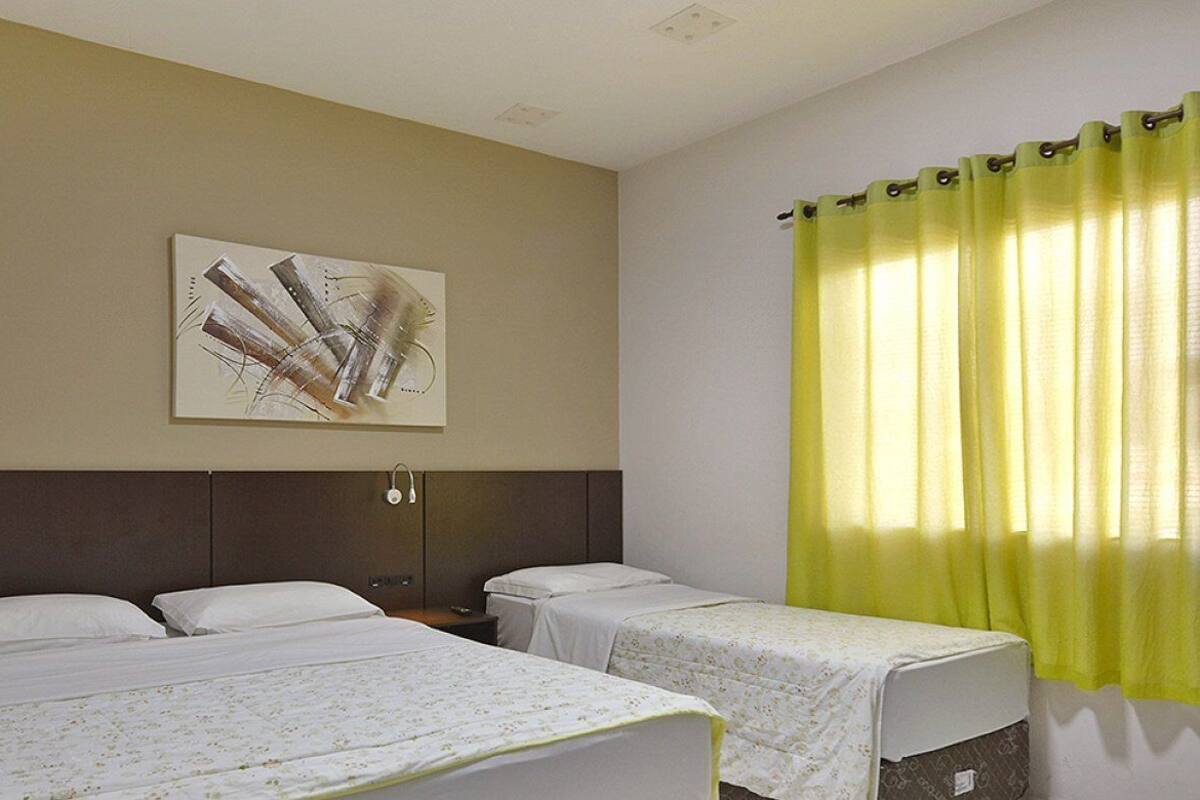 Habitación de hotel con dos camas individuales, cabecero, obra de arte colgada en la pared y ventana con cortinas amarillas.