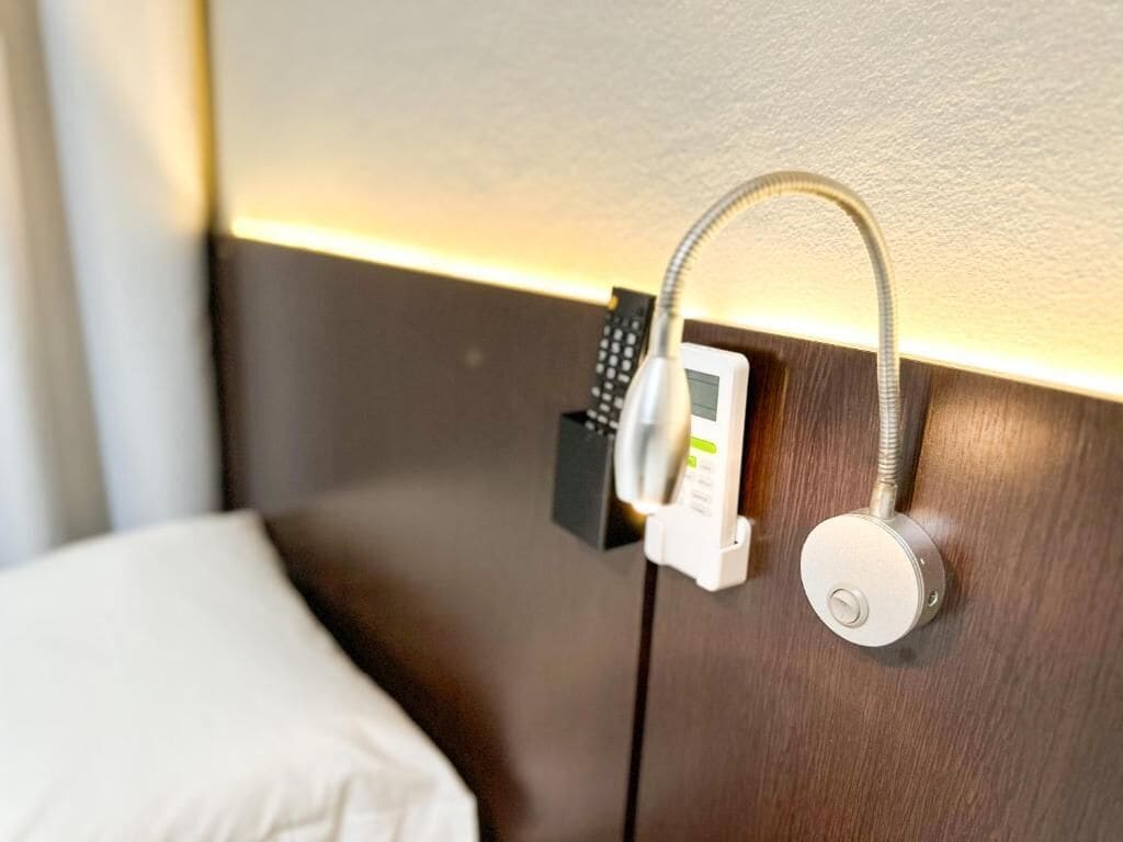 A hotel room with a bed, a control panel, and a wall-mounted device.