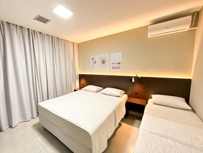 Habitación de hotel con dos camas, un ventanal con cortinas y obras de arte colgadas en la pared.