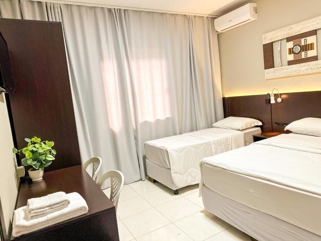 Een hotelkamer met twee bedden, een bureau met stoel, een potplant en een wandairconditioner.