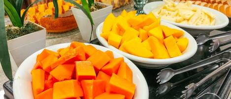 A buffet table with various dishes including cubed mangoes, a glass dessert dish, and other food items.