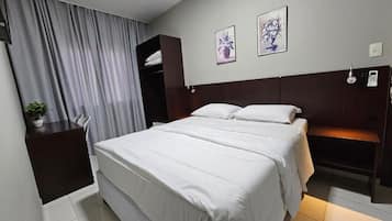 Quarto de hotel com cama, mesa de cabeceira, guarda-roupa e duas pinturas penduradas na parede.