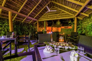 An outdoor dining area with thatched roof, wicker furniture, and a variety of dishes on the tables. - Sabba Summer Suite Maldives (Fodhdhoo)