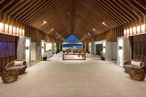 Um hall amplo com teto de madeira alto, áreas de estar confortáveis e vista para a cidade através de uma grande janela.