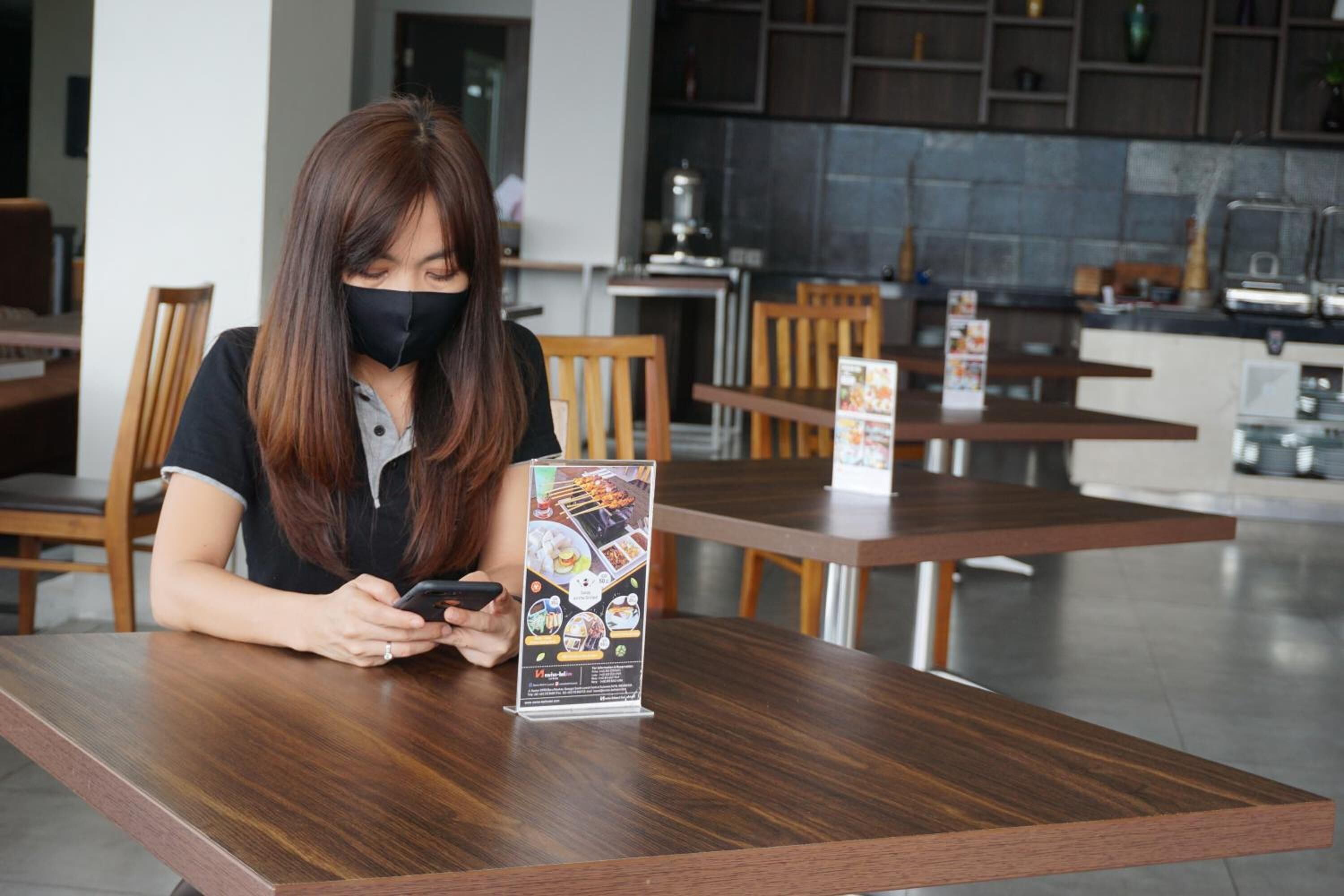 Una persona sentada a una mesa de madera en un ambiente interior moderno, posiblemente una cafetería o restaurante, con un atril de menú frente a ella.