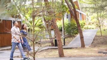 A couple walking on a paved path surrounded by trees and a building with a sloped roof.