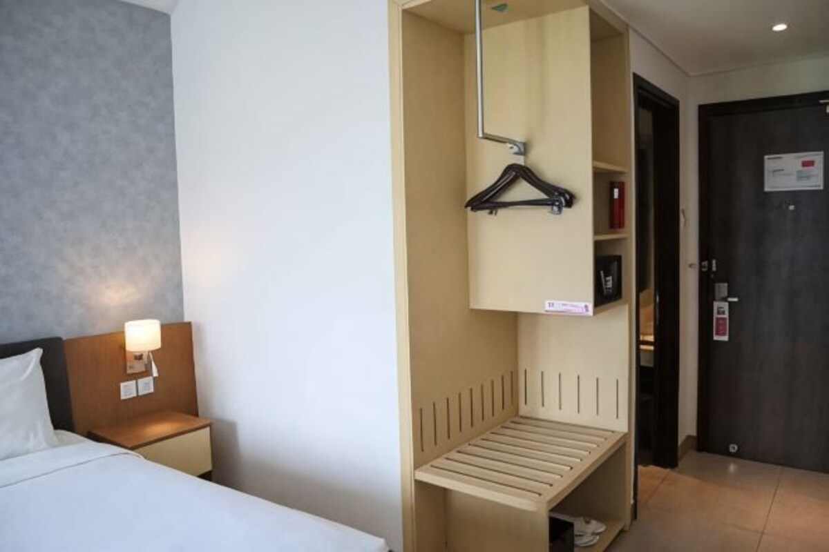 A hotel room with a bed, bedside lamp, wardrobe, and a door with a sign.