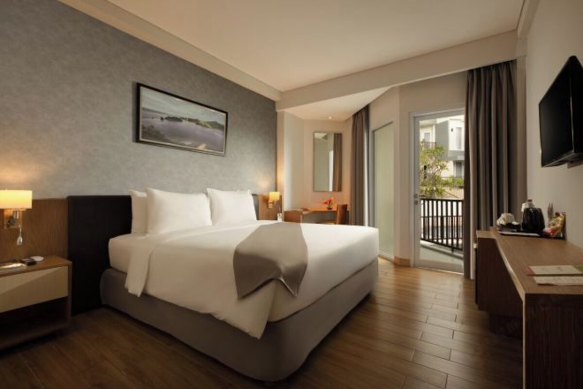 A hotel room with a large bed, a desk, a TV, and a balcony with a view.