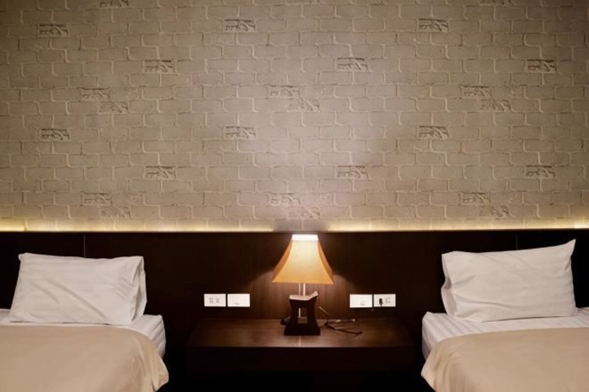 Une chambre d’hôtel avec un mur décoré d’un motif en briques, une table de chevet avec une lampe et deux lits.
